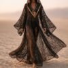 ZEVQ premium black lace hooded kaftan, a sheer festival kimono with gold trim, worn at a desert festival.