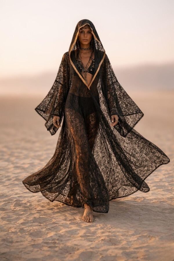 ZEVQ premium black lace hooded kaftan, a sheer festival kimono with gold trim, worn at a desert festival.
