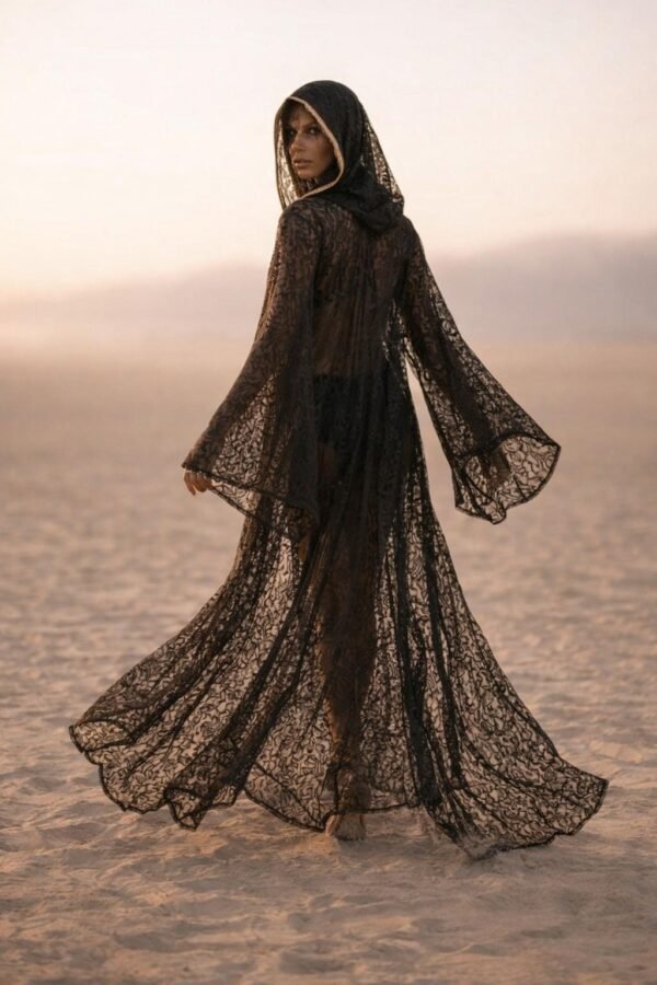 ZEVQ premium black lace hooded kaftan, a sheer festival kimono with gold trim, worn at a desert festival.