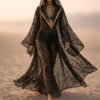 ZEVQ premium black lace hooded kaftan, a sheer festival kimono with gold trim, worn at a desert festival.