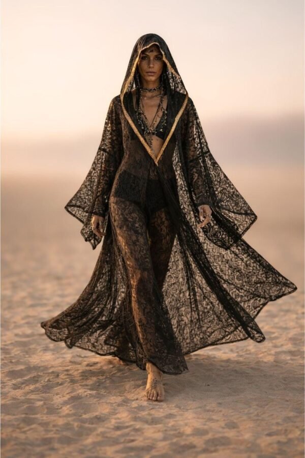 ZEVQ premium black lace hooded kaftan, a sheer festival kimono with gold trim, worn at a desert festival.