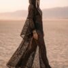 ZEVQ premium black lace hooded kaftan, a sheer festival kimono with gold trim, worn at a desert festival.